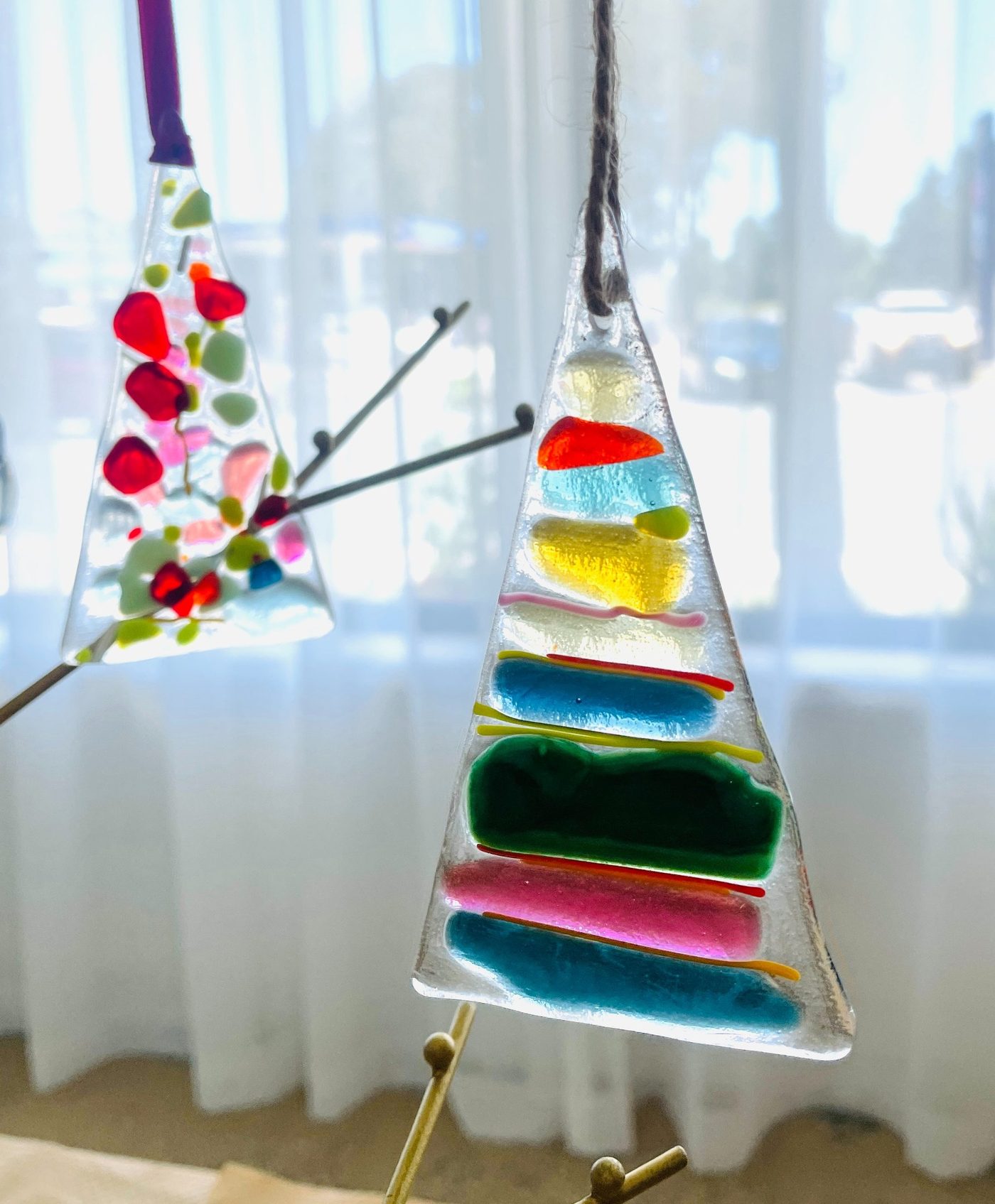 Fused glass Christmas tree ornaments hanging in the studio window